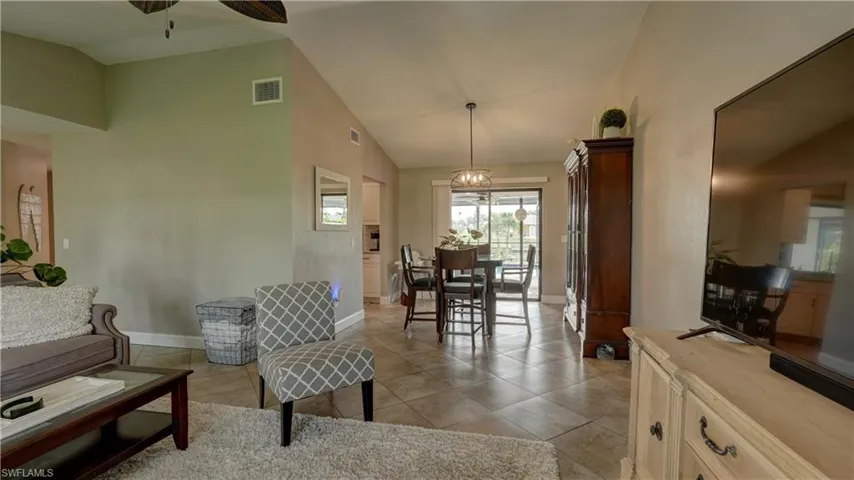 Vaulted ceiling living area featuring tile flooring, neutral wall paint, and a built-in ceiling fan