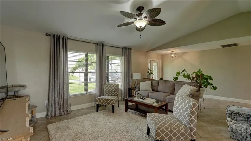 Vaulted ceilings featuring a ceiling fan with integrated lighting, tile flooring, and multiple windows with blinds
