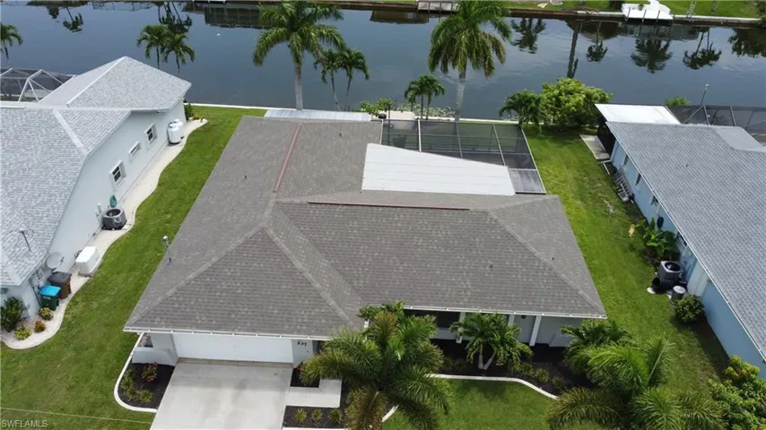 Waterfront property featuring a private boat dock, screened pool enclosure, mature palm trees, and an attached garage with concrete driveway