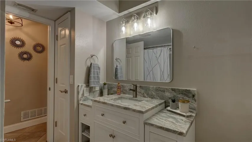 Bathroom featuring a white vanity with an undermount sink, a bronze-finish faucet, and a stone countertop with a matching backsplash