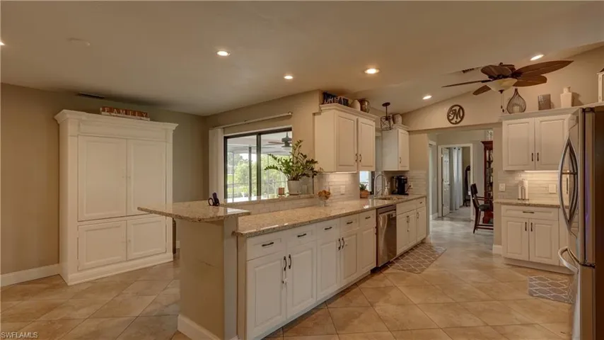 Spacious kitchen featuring white cabinetry, stone countertops, stainless steel appliances, tile flooring, and recessed lighting