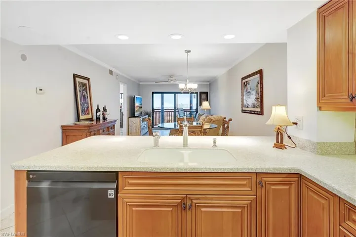 Kitchen with dishwashing machine, crown molding, a peninsula, light stone counters, and brown cabinetry