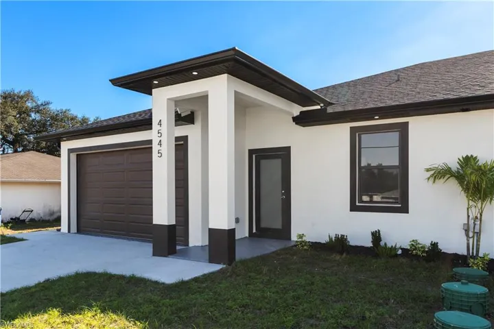 Entrance to property with a garage, roof with shingles, stucco siding, and a lawn