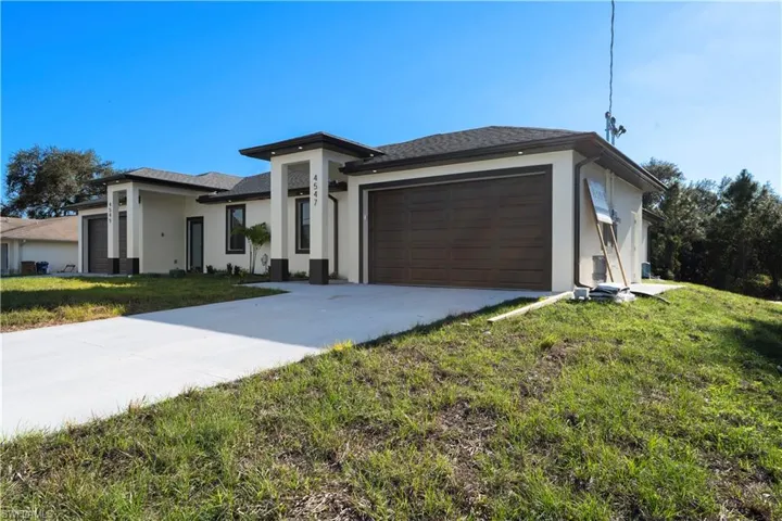 Prairie-style house with an attached garage, a front lawn, stucco siding, and concrete driveway