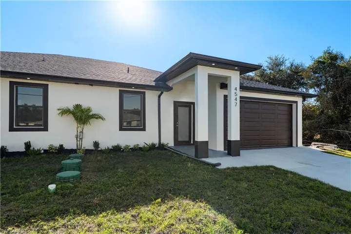 View of front of property with a front yard, a garage, driveway, stucco siding, and roof with shingles