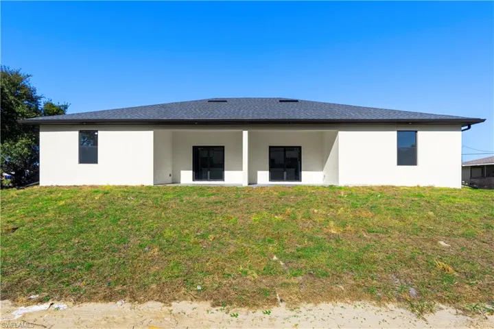 Rear view of property with stucco siding, a lawn, a patio area, and a shingled roof