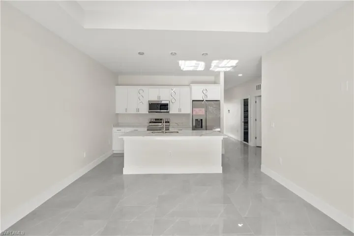 Kitchen featuring white cabinetry, a center island with sink, stainless steel appliances, and light stone countertops