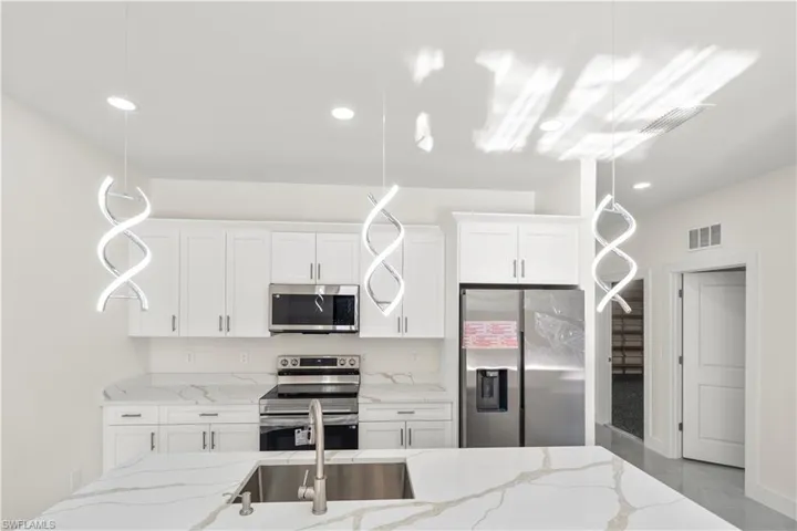 Kitchen with stainless steel appliances, light stone countertops, white cabinets, and decorative light fixtures
