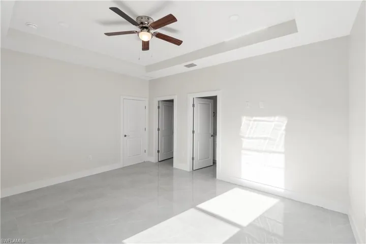 Unfurnished bedroom featuring a raised ceiling, ceiling fan, and light tile patterned floors