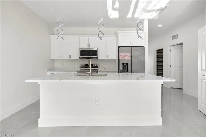 Kitchen featuring stainless steel appliances, white cabinets, an island with sink, light stone counters, and recessed lighting