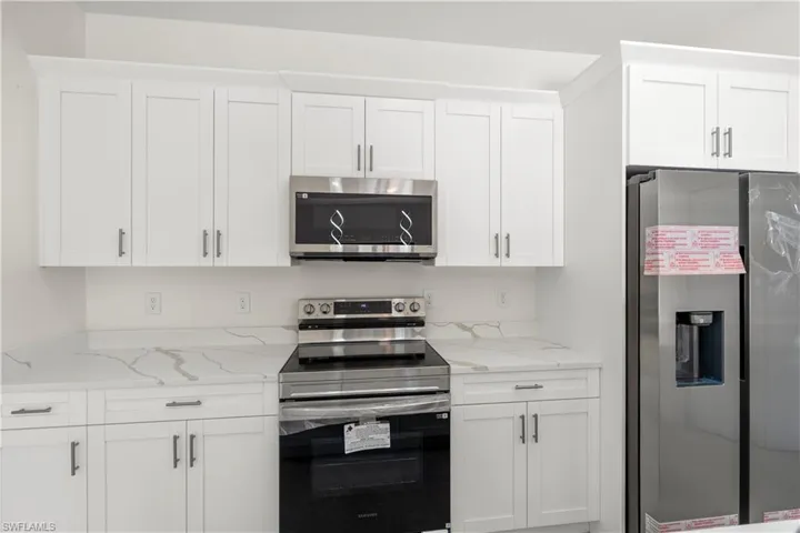 Kitchen featuring stainless steel appliances, white cabinets, and light stone counters
