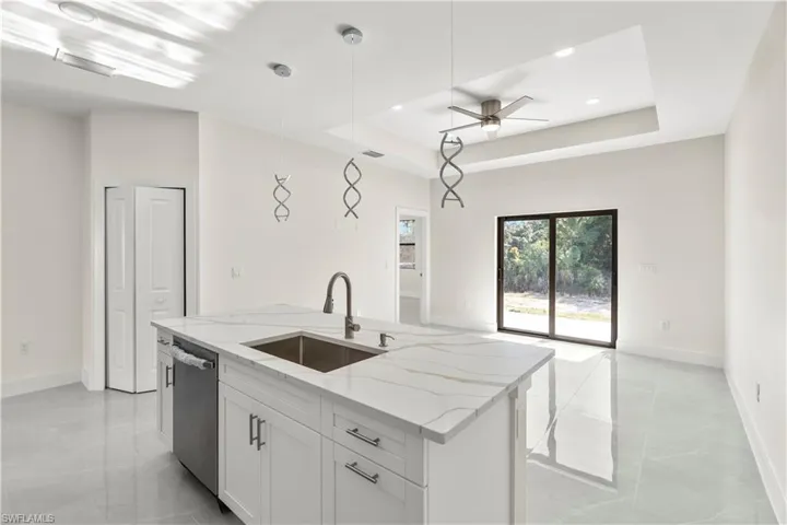 Kitchen featuring a tray ceiling, light stone counters, decorative light fixtures, a ceiling fan, and an island with sink