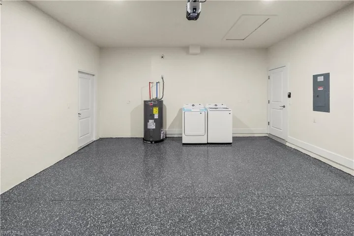 Misc room featuring electric panel, washing machine and clothes dryer, electric water heater, and light speckled floor