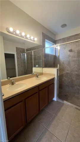 Bathroom featuring double vanity, a shower stall, and light tile patterned flooring