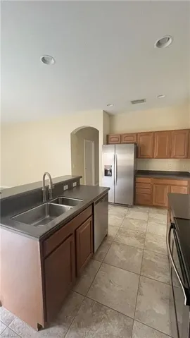 Kitchen featuring dark countertops, stainless steel appliances, a center island with sink, brown cabinetry, and recessed lighting