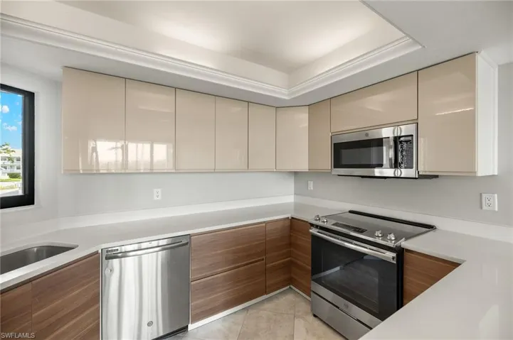 Kitchen with appliances with stainless steel finishes, light tile patterned floors, sink, a raised ceiling, and cream cabinets