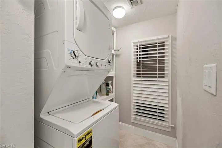 Laundry room featuring stacked washer and dryer, light tile patterned flooring, and a textured ceiling