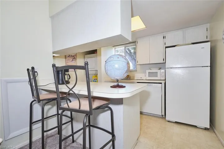 Kitchen featuring white appliances, light countertops, a kitchen bar, a peninsula, and light flooring