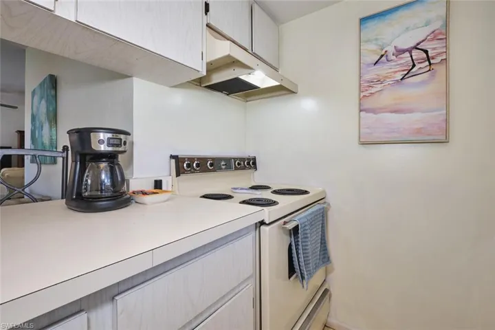 Kitchen featuring white range with electric cooktop, under cabinet range hood, and light countertops