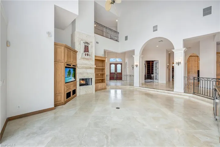 Living room featuring ceiling fan, built in features, decorative columns, a premium fireplace, and light tile patterned floors, bar area.