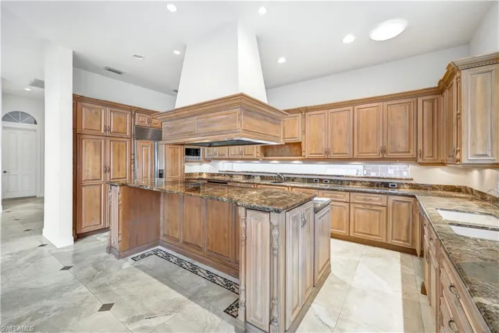 Kitchen featuring dark stone counters, a center island, light tile patterned floors, and custom range hood