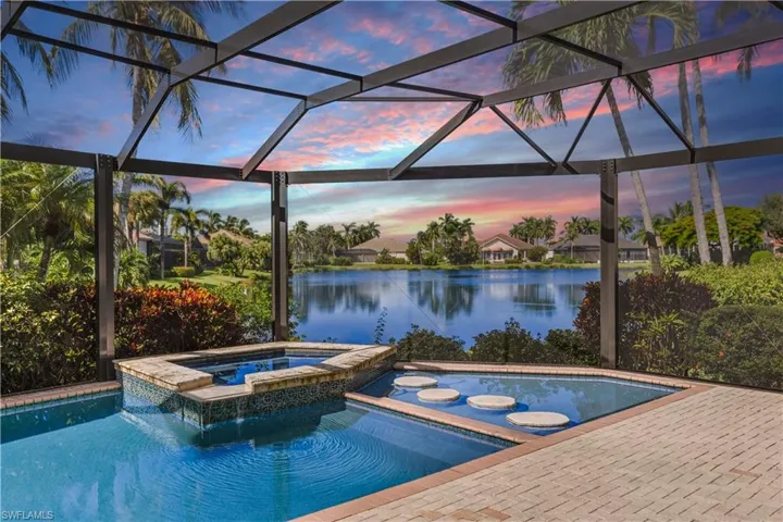 Pool at dusk featuring glass enclosure, a water view, and an in ground hot tub