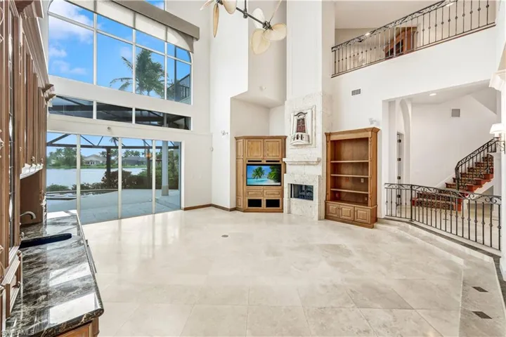 Living room featuring a 32 ft soaring high ceilings, built in shelves, a water view, fireplace, bar area, and light tile patterned floors