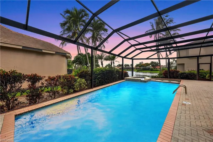 Pool at dusk featuring an in ground hot tub, a patio, and glass enclosure