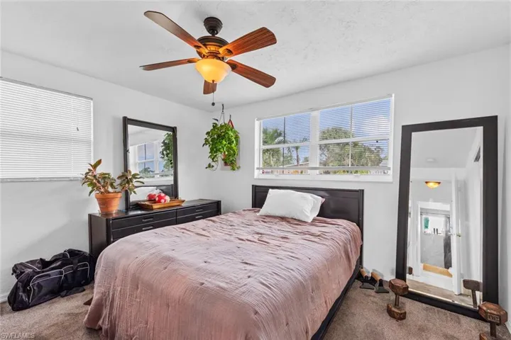 Carpeted bedroom featuring a textured ceiling, multiple windows, and ceiling fan