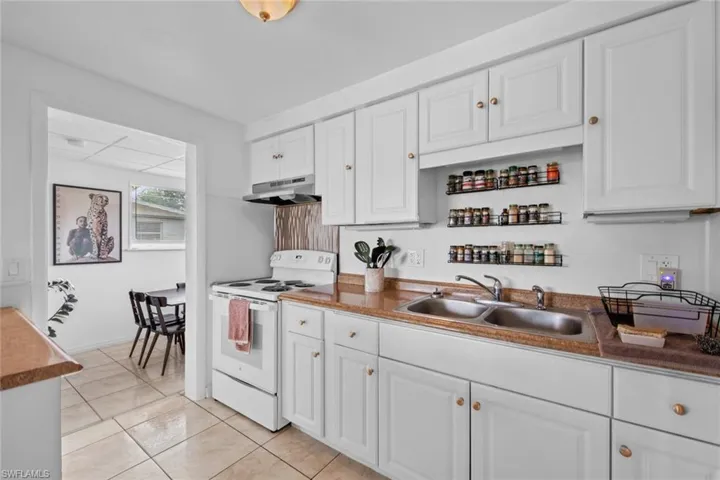 Kitchen featuring electric stove, sink, white cabinets, and light tile patterned floors