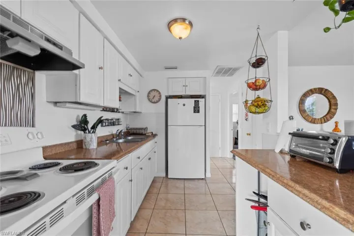 Kitchen featuring sink, white appliances, white cabinetry, and range hood