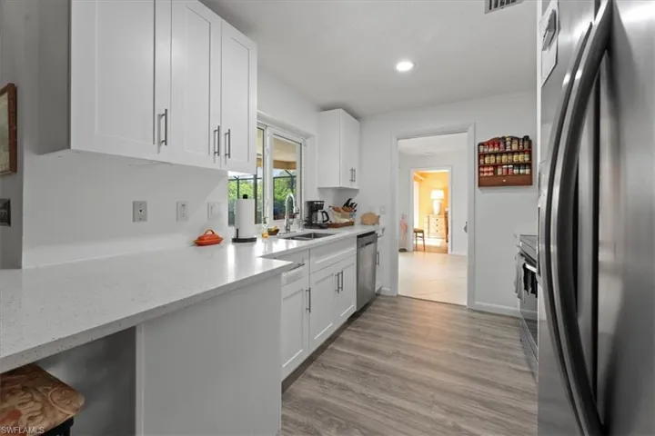 Kitchen with a sink, freestanding refrigerator, dishwasher, white cabinets, and light wood-style floors