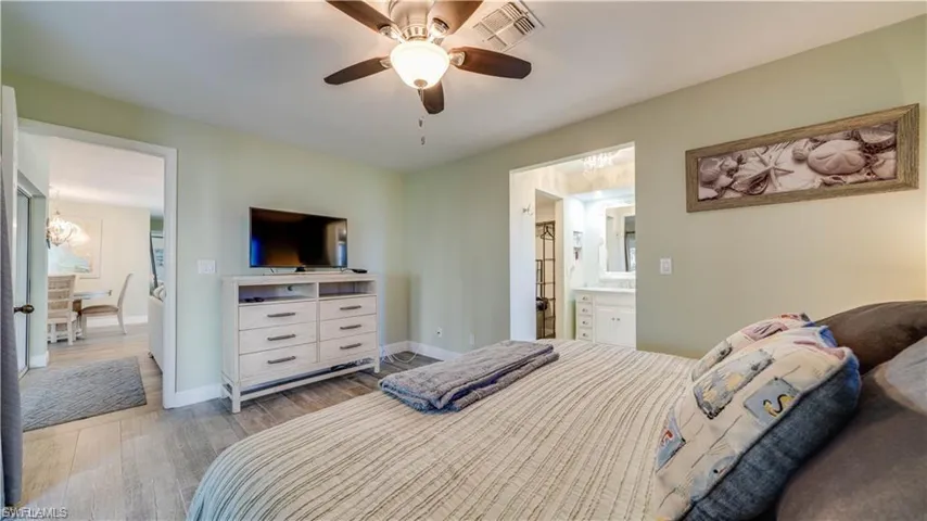 Bedroom with light wood-type flooring, a ceiling fan, and ensuite bath