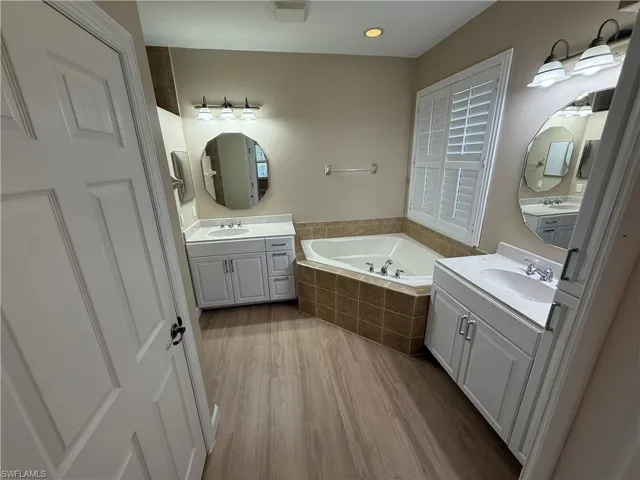 Full bath featuring two vanities, a garden tub, and light wood-style floors
