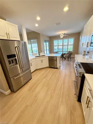 Kitchen featuring stainless steel appliances, a peninsula, white cabinetry, light wood-type flooring, and recessed lighting