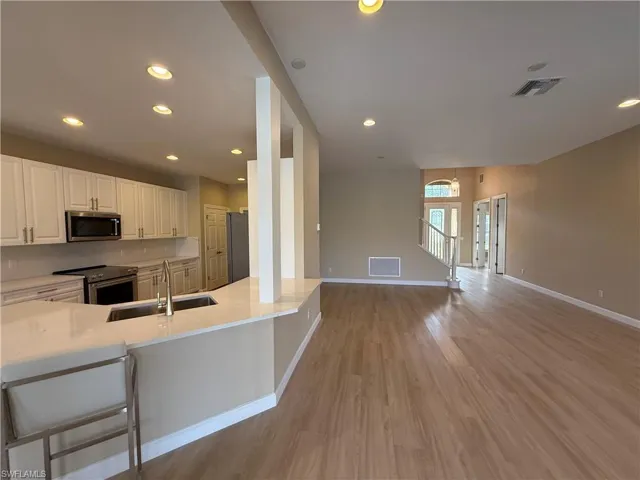 Kitchen with appliances with stainless steel finishes, open floor plan, a kitchen bar, white cabinets, and recessed lighting