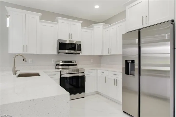 Kitchen with white cabinetry, light stone counters, stainless steel appliances, and sink
