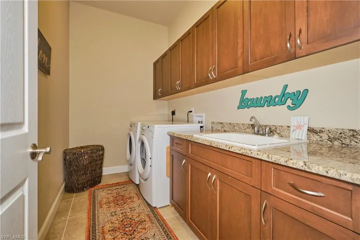 Laundry area with cabinets, light tile patterned floors, washer and dryer, and sink
