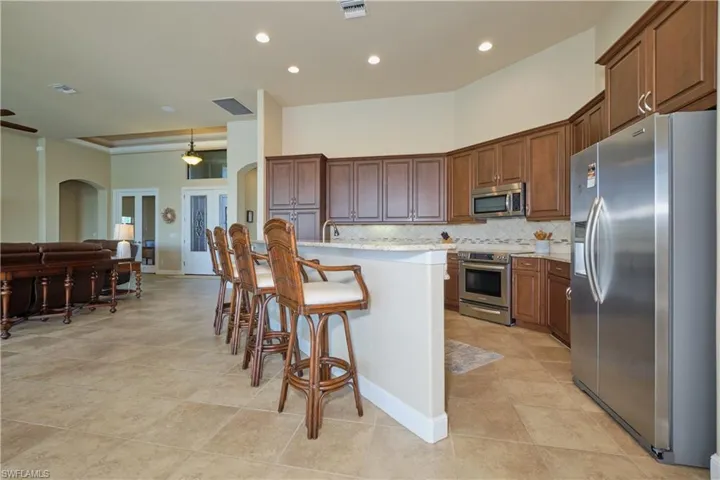 Kitchen featuring a breakfast bar, backsplash, light stone countertops, stainless steel appliances, and a center island