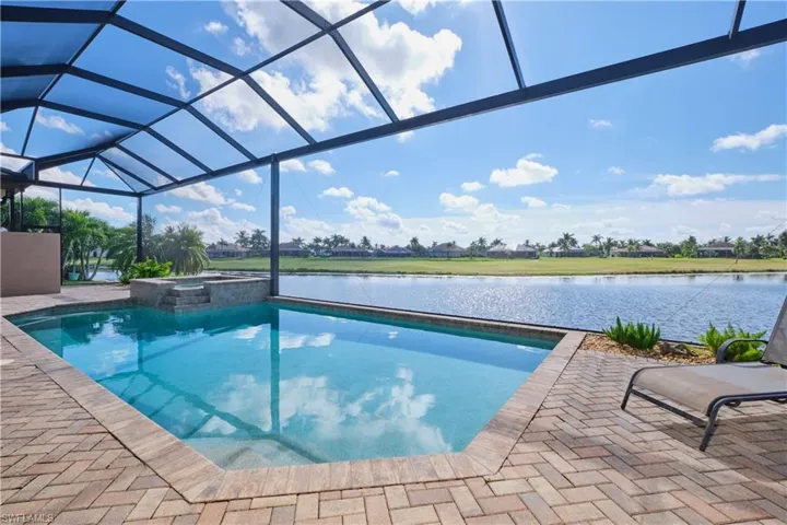View of pool with a water view, an in ground hot tub, a patio area, and glass enclosure