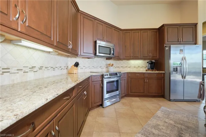Kitchen with appliances with stainless steel finishes, backsplash, light tile patterned flooring, and light stone countertops