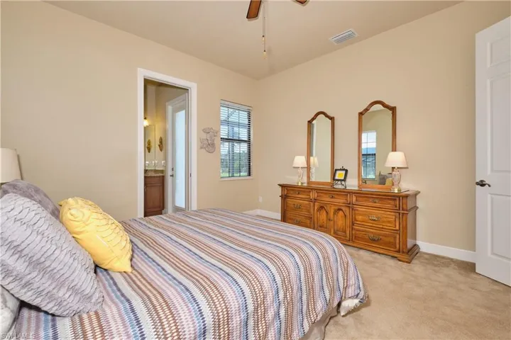 Bedroom featuring ceiling fan, light colored carpet, and ensuite bath