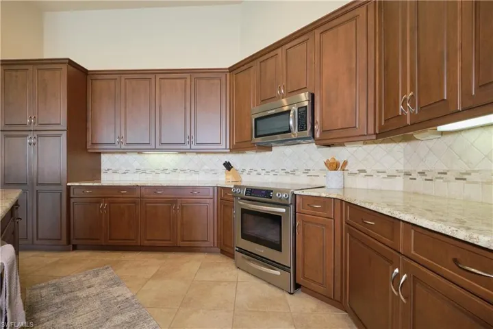 Kitchen with light stone counters, appliances with stainless steel finishes, light tile patterned floors, and decorative backsplash