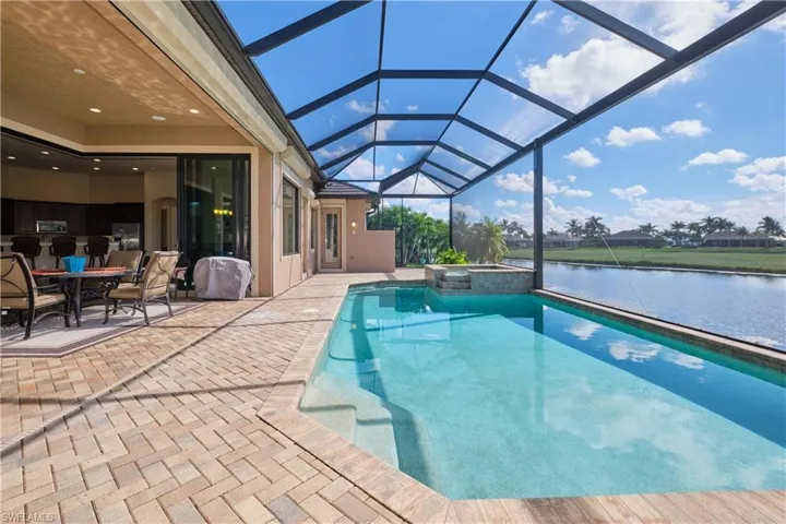 View of pool featuring a water view, an in ground hot tub, a patio area, and glass enclosure