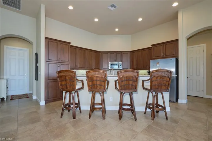 Kitchen with a kitchen breakfast bar, a center island with sink, appliances with stainless steel finishes, light tile patterned floors, and light stone countertops