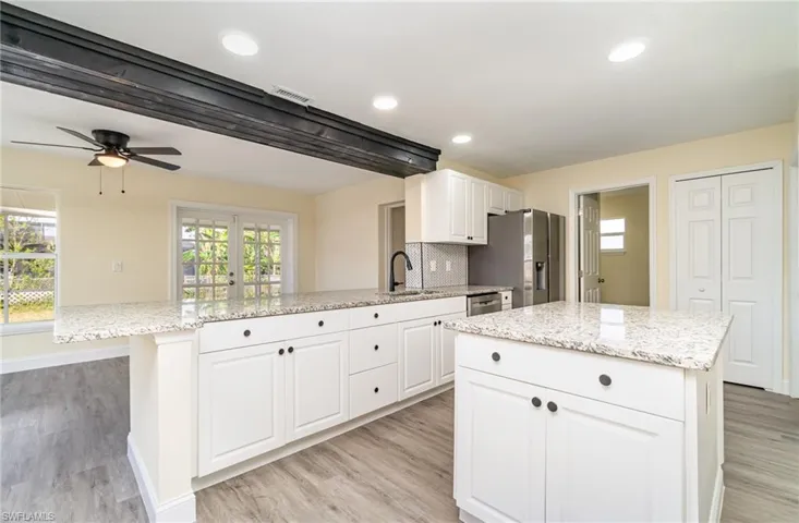 Kitchen with light stone countertops, white cabinets, a center island, decorative backsplash, and recessed lighting
