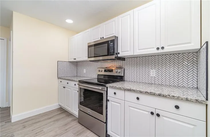Kitchen featuring appliances with stainless steel finishes, white cabinetry, tasteful backsplash, light stone countertops, and light wood finished floors