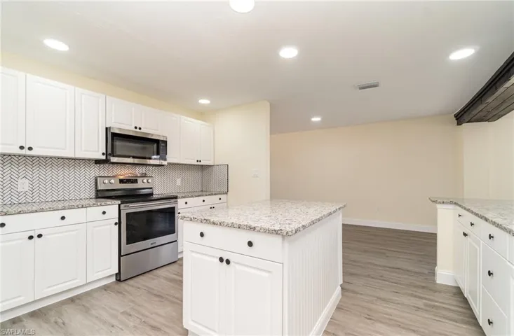 Kitchen with white cabinets, appliances with stainless steel finishes, backsplash, a center island, and recessed lighting