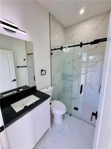 Full bath featuring vanity, a marble finish shower, light marble finish floors, and recessed lighting