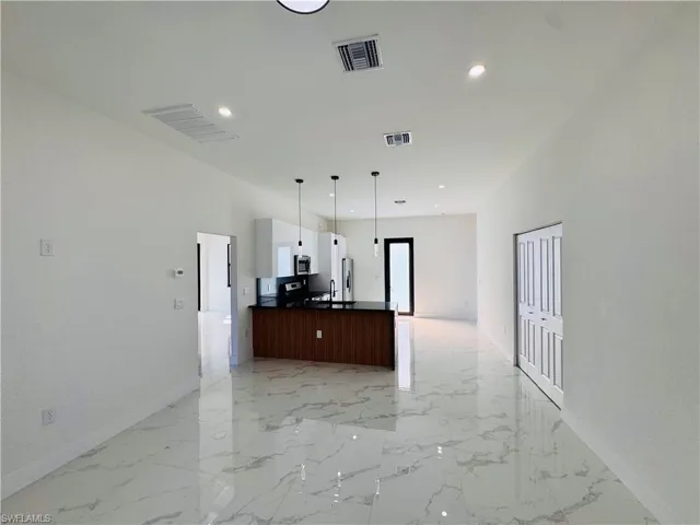 Kitchen featuring open floor plan, decorative light fixtures, light marble finish flooring, recessed lighting, and white cabinets